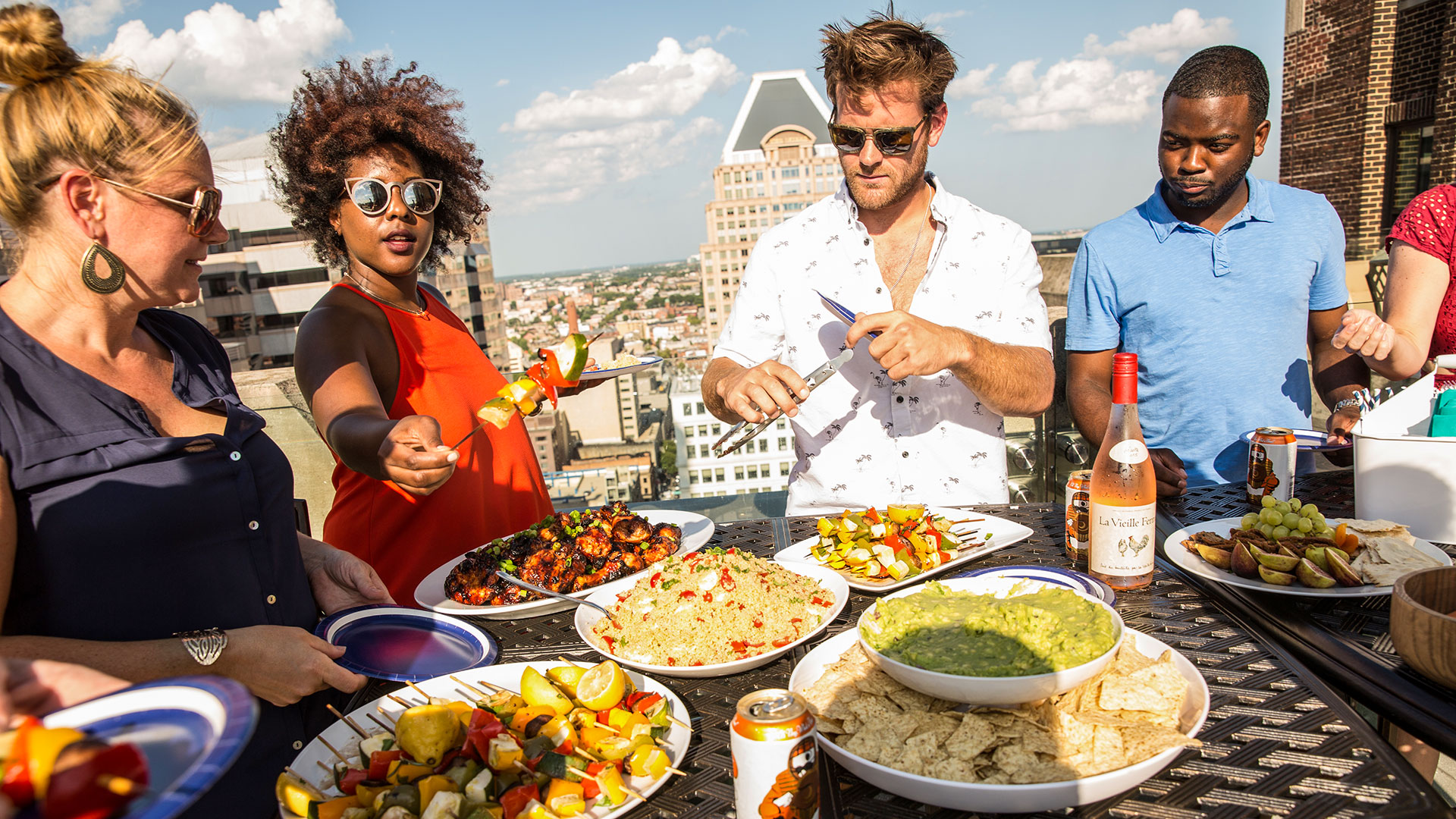 Diverse group of four people at rooftop party with food.