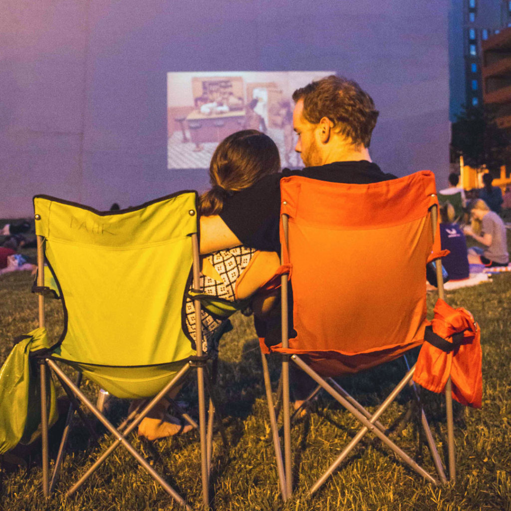 Couple sits in folding, stadium chairs and cuddles up in front of an outdoor movie projection in Bromo Arts District of Baltimore.