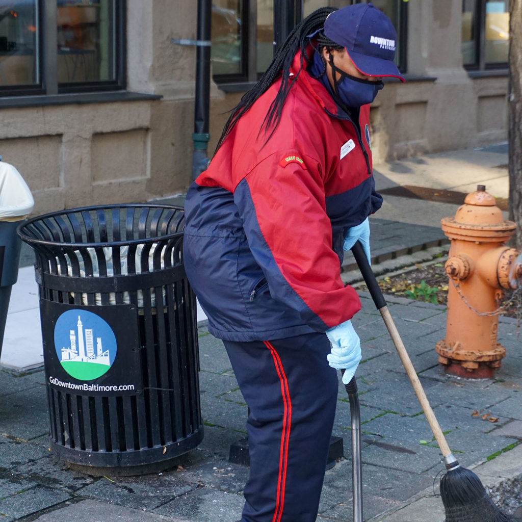 Woman in uniform, sweeping city sidewalk.