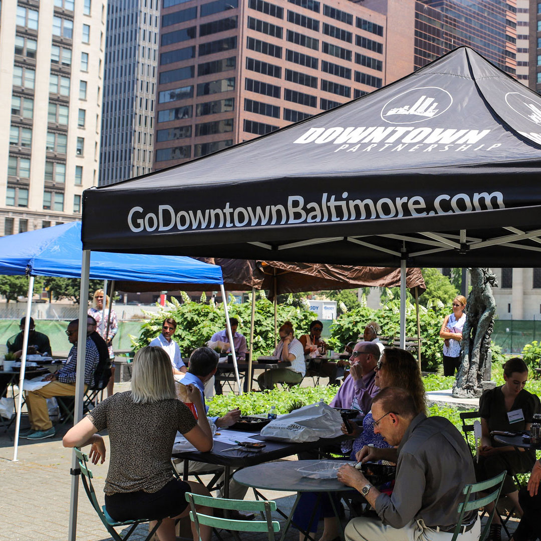 People eating in Downtown Baltimore plaza under shaded canopy tents during networking event.