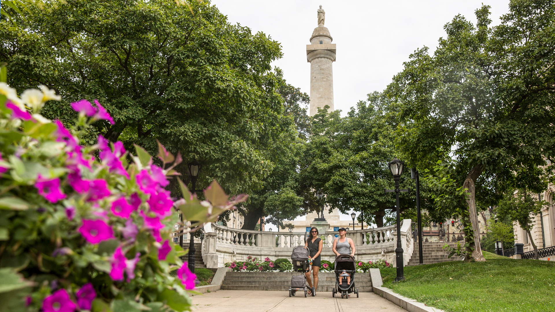 Two women pushing strollers in front of Washington Monument in Mt. Vernon Baltimore in the spring. In Baltimore, you can climb to the top of the Mt. Vernon Monument.