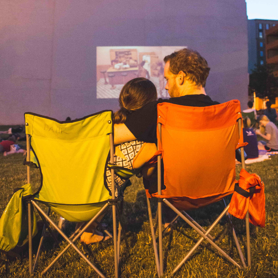 Couple sits in lawn chairs at outdoor movie screening.